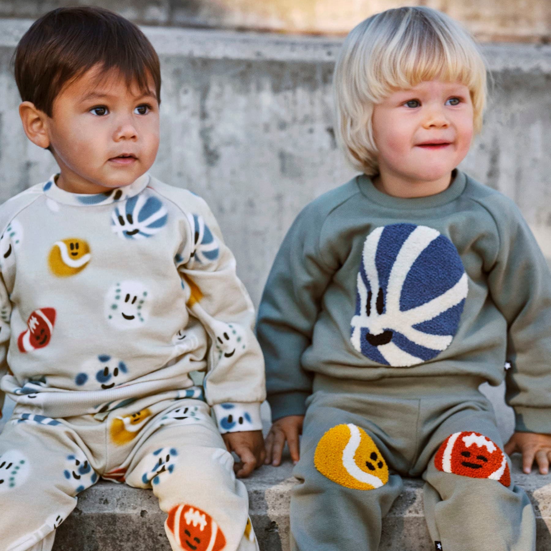 Two children wearing colorful outfits sitting on a stone surface.